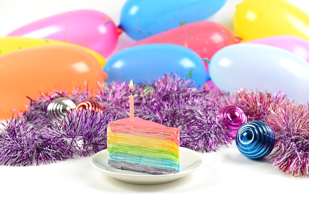 Photo gâteau arc-en-ciel anniversaire avec bougie sur fond de ballons de fête.