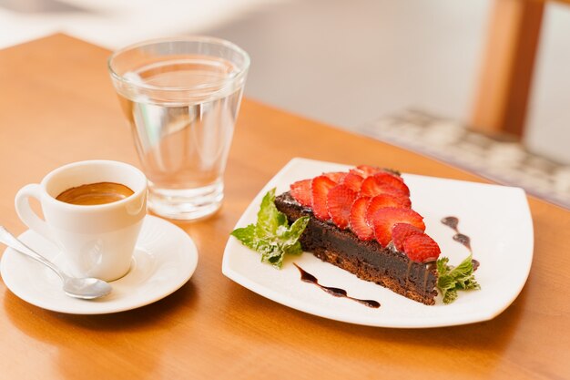 Gâteau au chocolat, brownie aux fraises et menthe, expresso, verre d'eau sur une table en bois