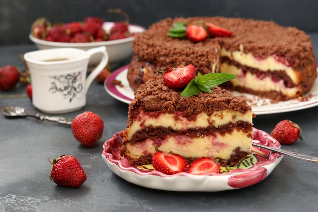 Gâteau au chocolat avec du fromage cottage aux fraises est situé sur une surface sombre, un morceau de gâteau est situé au premier plan sur une plaque