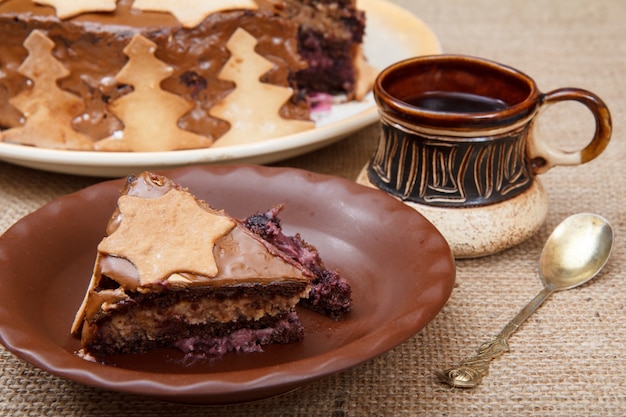 Gâteau au chocolat fait maison décoré d'ornements de Noël, tasse d'argile de café noir et cuillère sur table avec un sac.