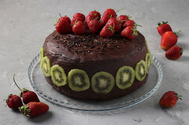 Gâteau au chocolat maison décoré de fraises et de kiwi situé sur fond de béton gris, format horizontal, gros plan