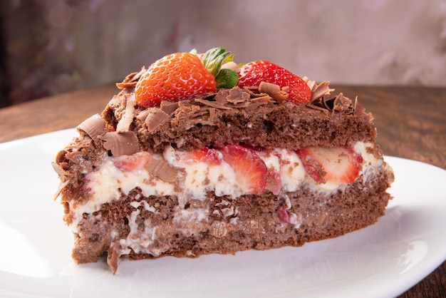 Gâteau au chocolat, une savoureuse tranche de gâteau au chocolat avec des fraises sur une plaque blanche sur bois rustique, fond abstrait, mise au point sélective.