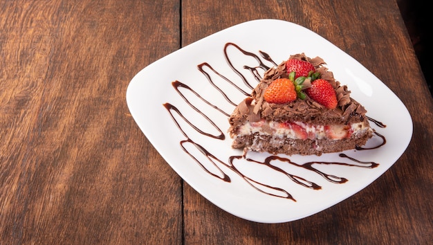Gâteau au chocolat, une savoureuse tranche de gâteau au chocolat avec des fraises sur une plaque blanche sur bois rustique, fond abstrait, mise au point sélective.