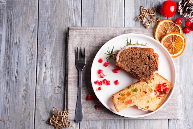 Gâteau Au Chocolat En Tranches De Noël Et Gâteau Aux Fruits Avec Plaque De Pépins De Grenade Et De Glaçage Blanc à Décor Sur Un Fond En Bois Gris, Plat