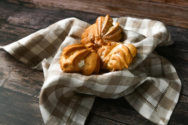 Gâteau au choux sur un bois. Dans un panier sur une serviette à carreaux. L'appartement était couché. . Chic avec du fromage cottage. Petits gâteaux à la crème dans un bol en osier sur bois