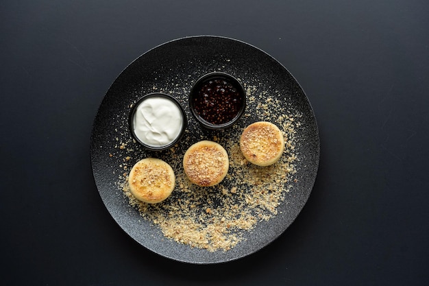 Photo gâteau au fromage au fromage cottage dans une assiette noire avec de la crème sure et de la confiture