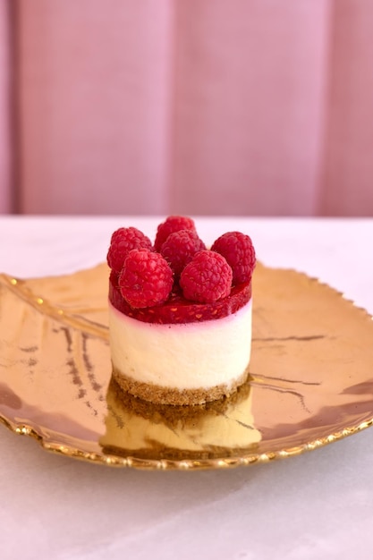 Gâteau au fromage aux framboises sur fond rose plaque dorée