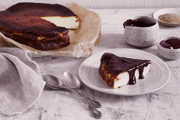 Gâteau au fromage brûlé basque sur papier parchemin avec morceau coupé sur l'assiette recouverte de chocolat avec serviette servie avec chocolat et confiture