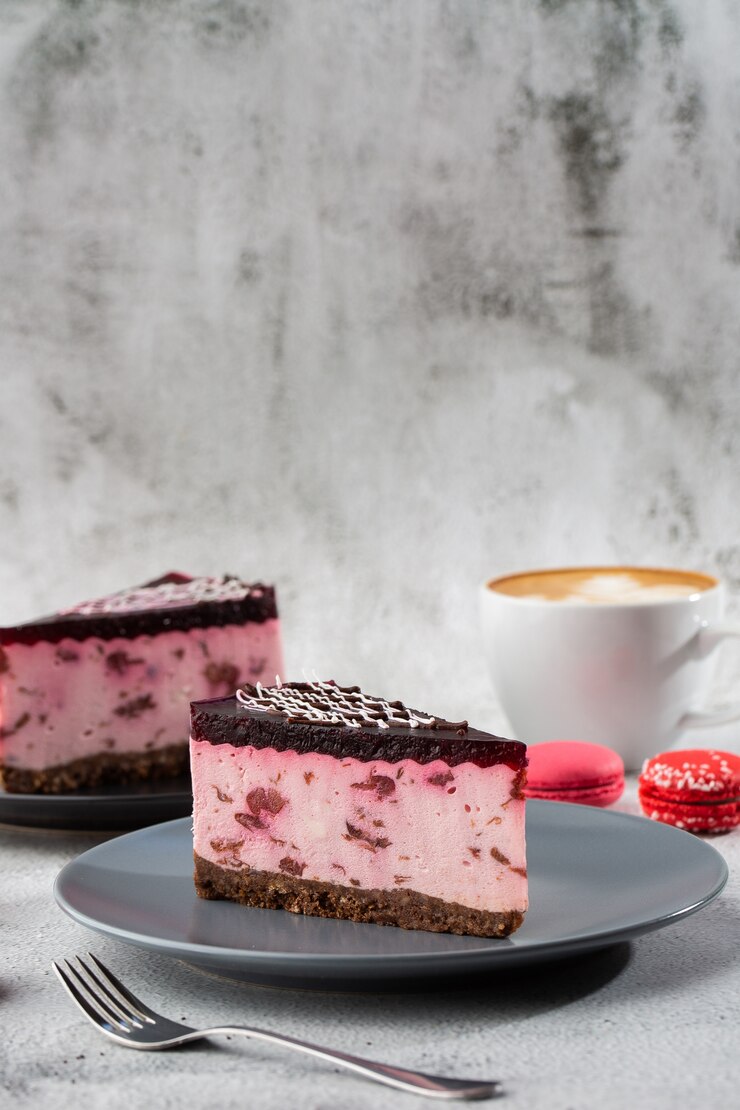 Gâteau au fromage avec cerise avec une tasse de café sur le tableau blanc. Vue rapprochée. Petit déjeuner savoureux. Morceau de gâteau sur plaque noire, tasse blanche sur fond de marbre blanc. Photo verticale.