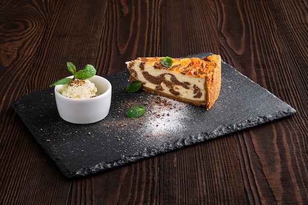 Gâteau au fromage en couches avec de la crème glacée servi sur une plaque d'ardoise sur une table en bois foncé