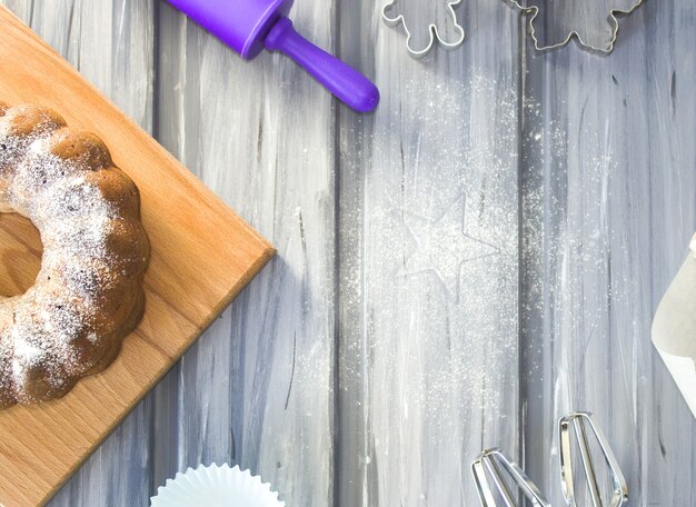 Gâteau au sucre en poudre, rouleau à pâtisserie, moules, parchemin, fouet et farine sur fond gris