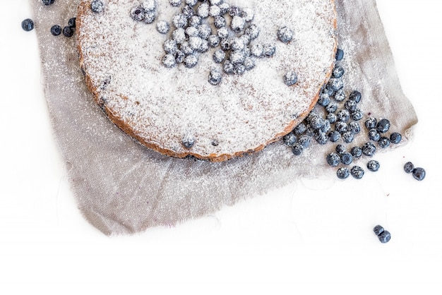 Gâteau aux bleuets avec des bleuets frais et du sucre en poudre sur un tissu beige sur une surface blanche