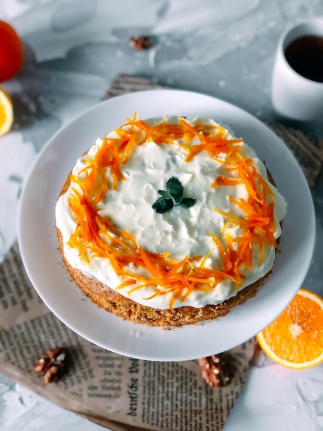 Gâteau Aux Carottes Sur Une Assiette Blanche Avec Une Demi-coupe D'orange Et Une Tasse De Café Sur Fond De Marbre Clair