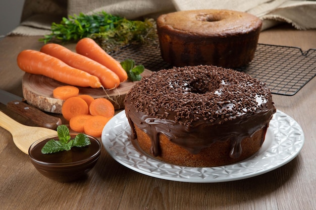 Gâteau aux carottes brésilien avec glaçage au chocolat sur une table en bois avec des carottes en arrière-plan