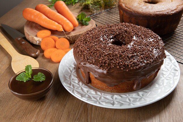 Gâteau aux carottes brésilien avec glaçage au chocolat sur une table en bois avec des carottes en arrière-plan