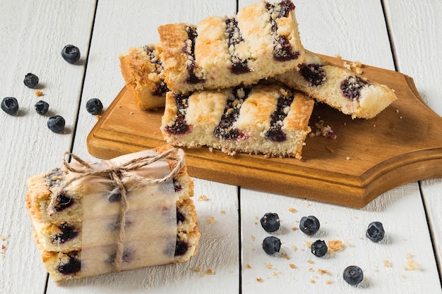 Gâteau aux carreaux avec de la confiture de bleuets sur une planche et une pile, attaché un garrot, bleuets sur fond de bois blanc