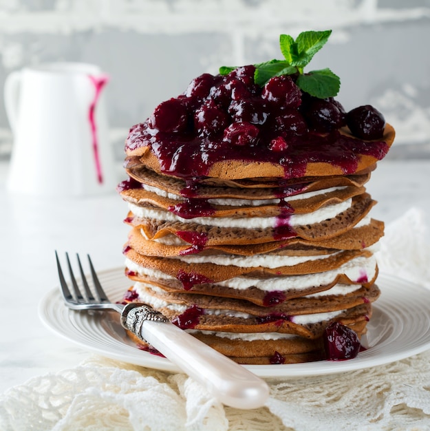 Gâteau aux crêpes au chocolat avec garniture au fromage cottage et sauce aux cerises sur fond clair. Mise au point sélective.