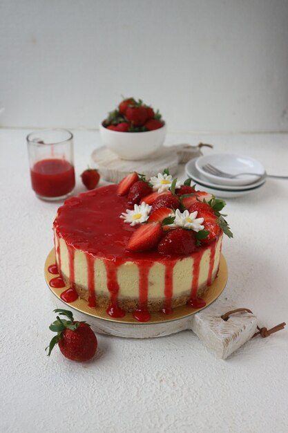 Photo gâteau aux fraises garni de fleurs blanches de confiture rouge et de fraises tranchées sur une table en bois blanc