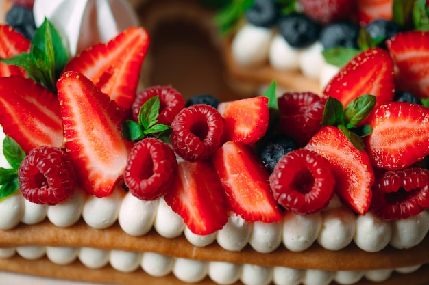 Gateau aux fruits Gâteau décoré avec des baies sur un support en bois sur un fond noir.