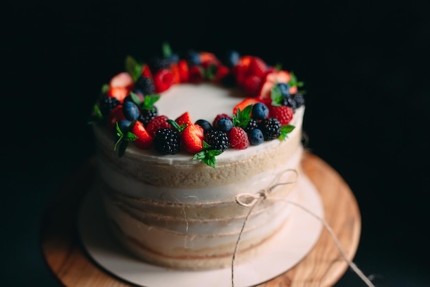 Gâteau aux fruits. Gâteau décoré de baies sur un support en bois sur fond noir.