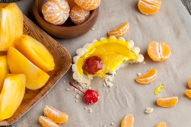 Gâteau aux fruits avec gelée et fruits divers, pêche, raisins, cerises, à côté des gâteaux mandarines et oranges