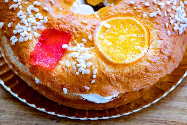 Gâteau aux fruits rond de Noël décoré de branche de sapin, fruits glacés et noix sur une table en bois.