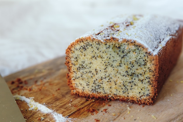 Gâteau aux graines de pavot et au zeste de citron, saupoudré de sucre en poudre. Petit gâteau au citron sur une planche de bois.