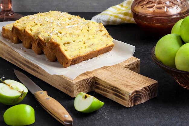 Gâteau aux pommes en tranches et à la noix de coco sur une planche à découper en bois sur fond sombre