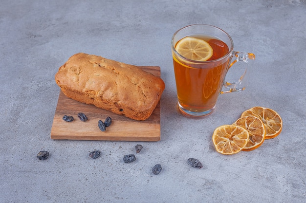 Gâteau aux raisins secs et tasse de thé avec du citron tranché sur une surface en marbre.