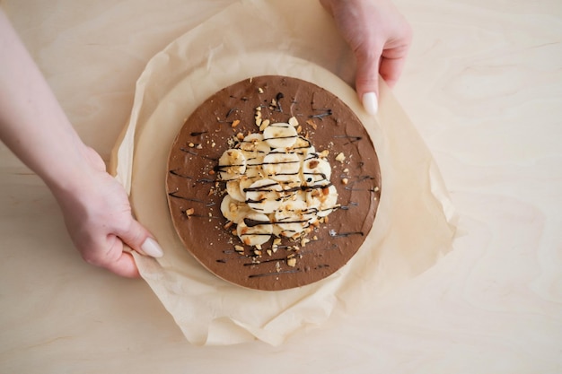 Gâteau à la banane au chocolat fait maison avec les mains sur du papier parchemin Livraison de nourriture Cuisson maison Vue de dessus Délicieuse tarte au chocolat et à la banane sur la table en bois