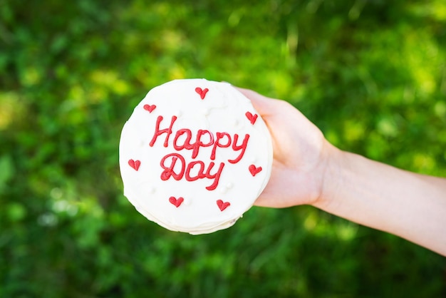 Gâteau bento avec l'inscription happy day et coeurs rouges une fille tient un gâteau à la main sur un fond d'herbe verte Journée ensoleillée Mise au point sélective