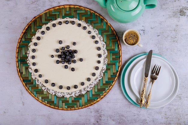 Gâteau blanc avec bleuets frais sur le dessus, café et assiettes.