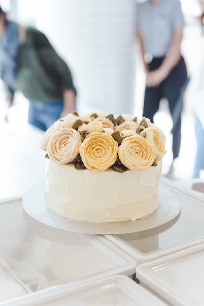 Gâteau blanc avec des fleurs de crème de beurre décorées sur un support.