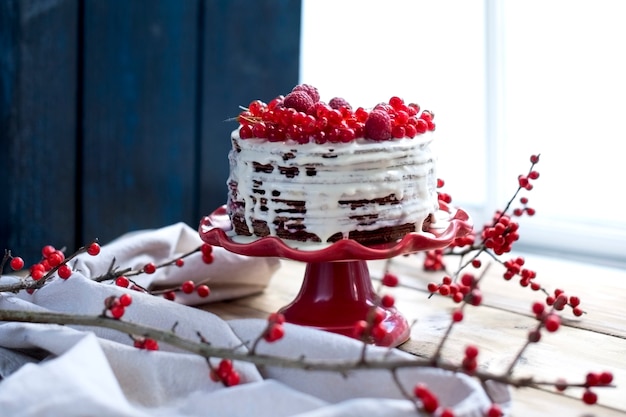 gâteau blanc avec des fruits rouges et une branche sur la table près de la fenêtre