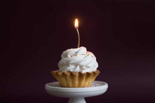 Gâteau avec bougie rose sur un support blanc sur fond sombre