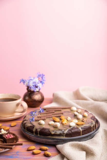 Gâteau brownie au chocolat fait maison avec de la crème au caramel et des amandes avec une tasse de café sur un fond coloré et rose. Vue latérale, mise au point sélective, espace copie.