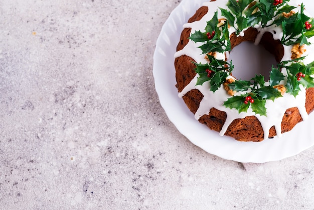 Gâteau Bundt au chocolat noir fait maison de Noël, décoré de glaçage blanc et de branches de baies de houx, un béton léger. Pose à plat