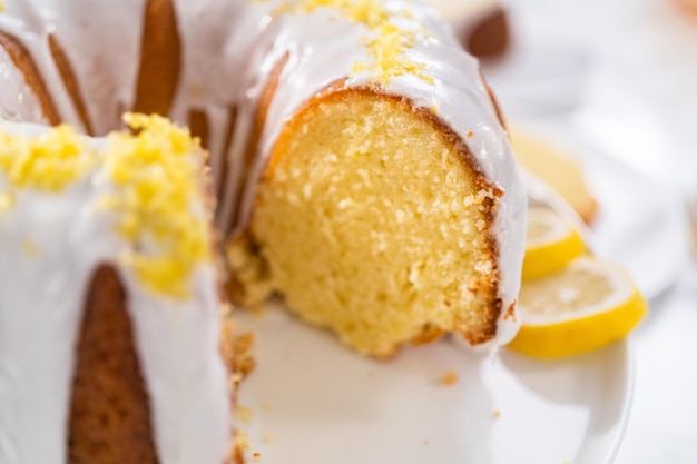 Gâteau bundt au citron tranché décoré de zeste de citron sur un support à gâteau.