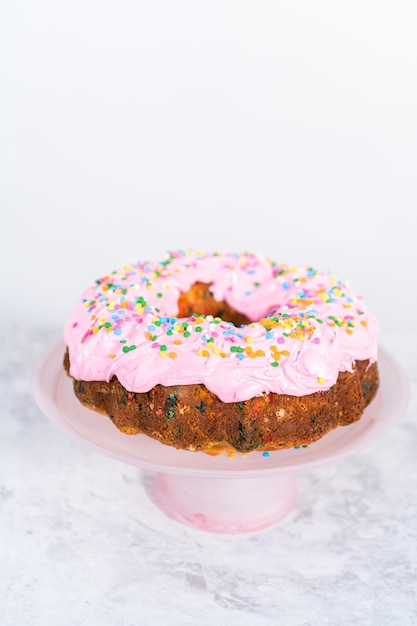 Gâteau Bundt Funfettti givré avec un glaçage à la crème au beurre à la vanille rose et décoré de paillettes arc-en-ciel