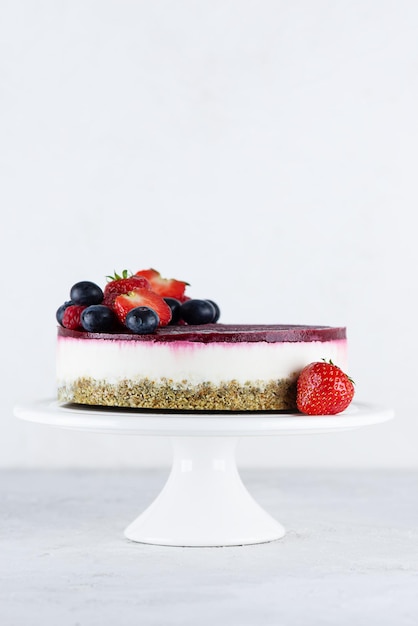 Gâteau de chou-fleur à la mousse crue avec des baies sur fond clair. Sans sucre, sans gluten, sans lactose, végétalien.