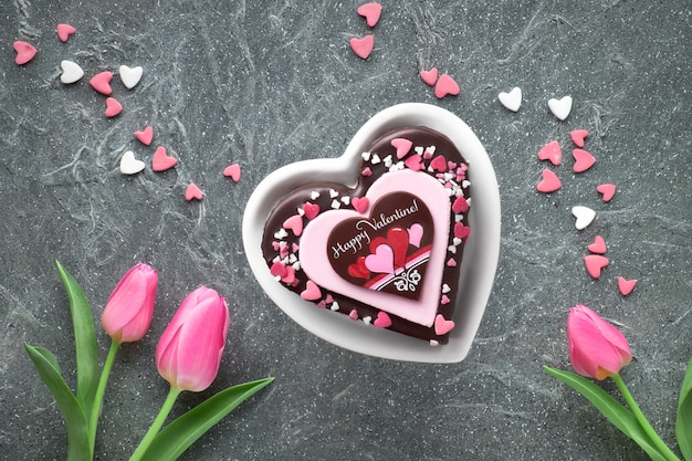 Gâteau coeur Saint Valentin avec des décorations en chocolat et sucre et texte de voeux "Happy Valeitine" et tulipes roses