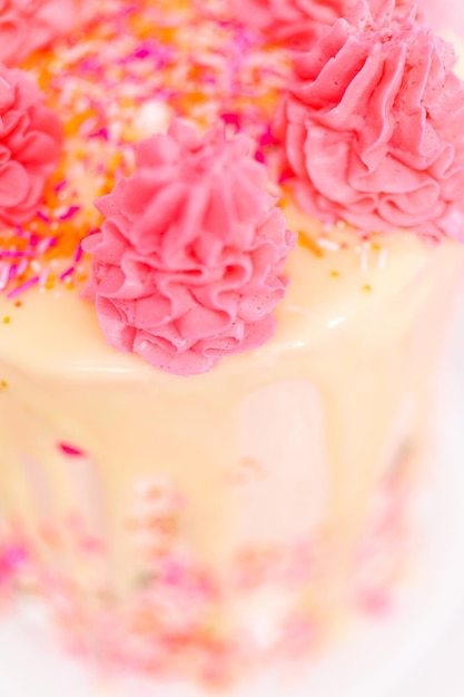 Gâteau à la crème au beurre rose et blanc avec pépites roses et goutte de ganache au chocolat blanc.