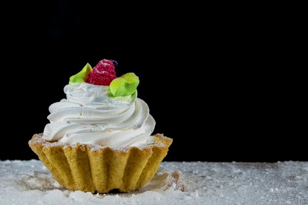 Gâteau à la crème blanche décoré de baies sur une planche de bois sur fond noir