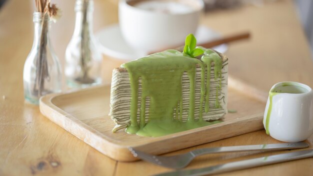 Un gâteau de crêpe au thé vert avec des feuilles de thé vert sur une assiette en bois