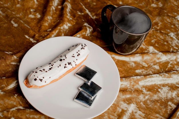 Gâteau éclair à la vanille sur une assiette sur fond d'or avec du café