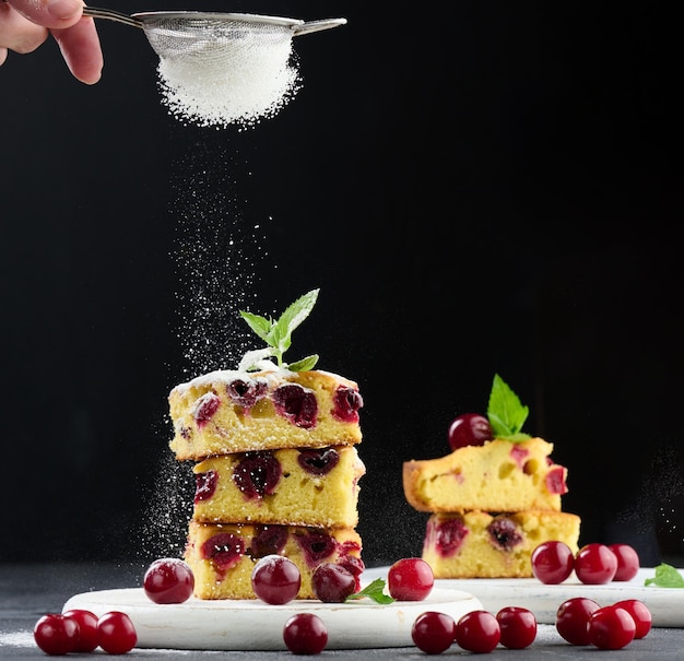 Gâteau d'éponge cuit au four avec des cerises saupoudrées de sucre en poudre sur fond noir