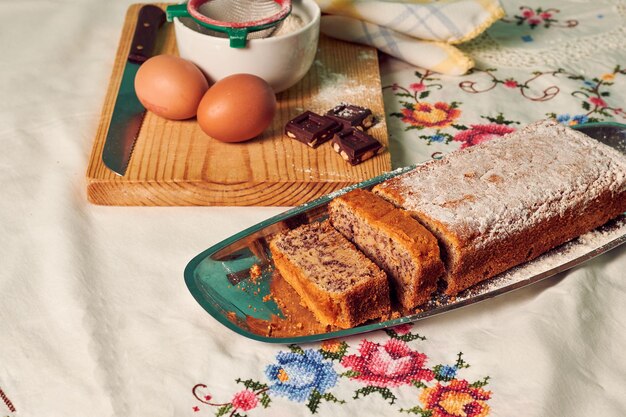 Gâteau éponge fait maison sur une nappe blanche avec quelques ingrédients oeufs chocolat et farine