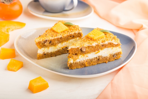 Gâteau fait maison avec kaki et citrouille et une tasse de café sur une surface en bois blanche avec textile orange. vue latérale, mise au point sélective.