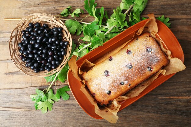 Gâteau fraîchement sorti du four avec des cassis dans une casserole brune sur table en bois, vue du dessus