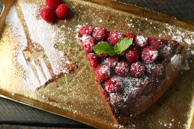 Gâteau avec glaçage au chocolat et framboises sur plateau en bois